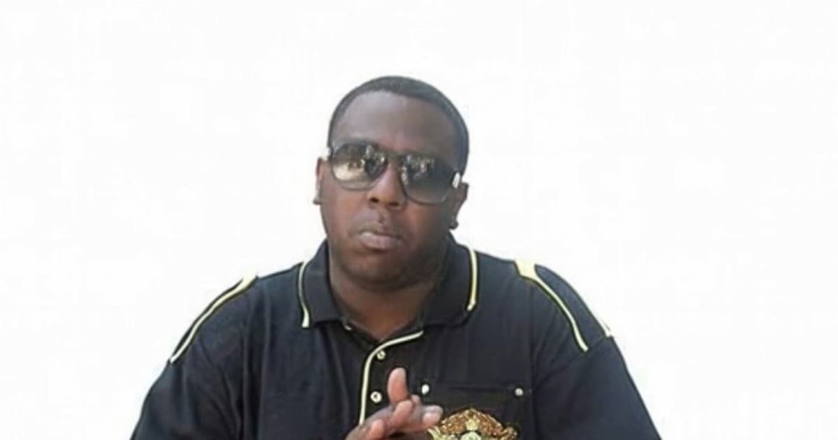 Benjamin Benz in a black polo with gold trim and dark sunglasses, photographed against a white studio background.