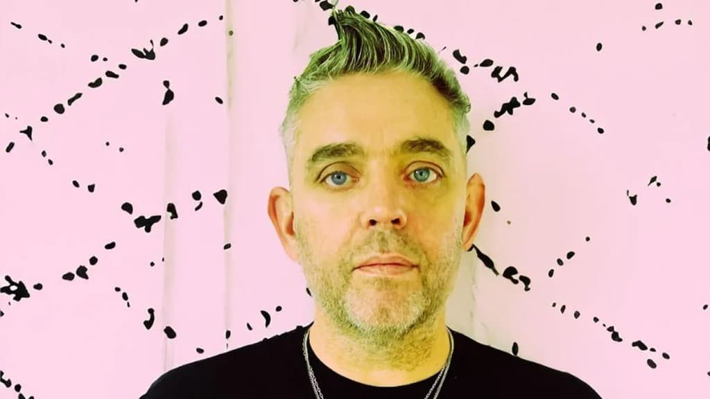 Def Nettle portrait against a pink backdrop with black abstract markings.