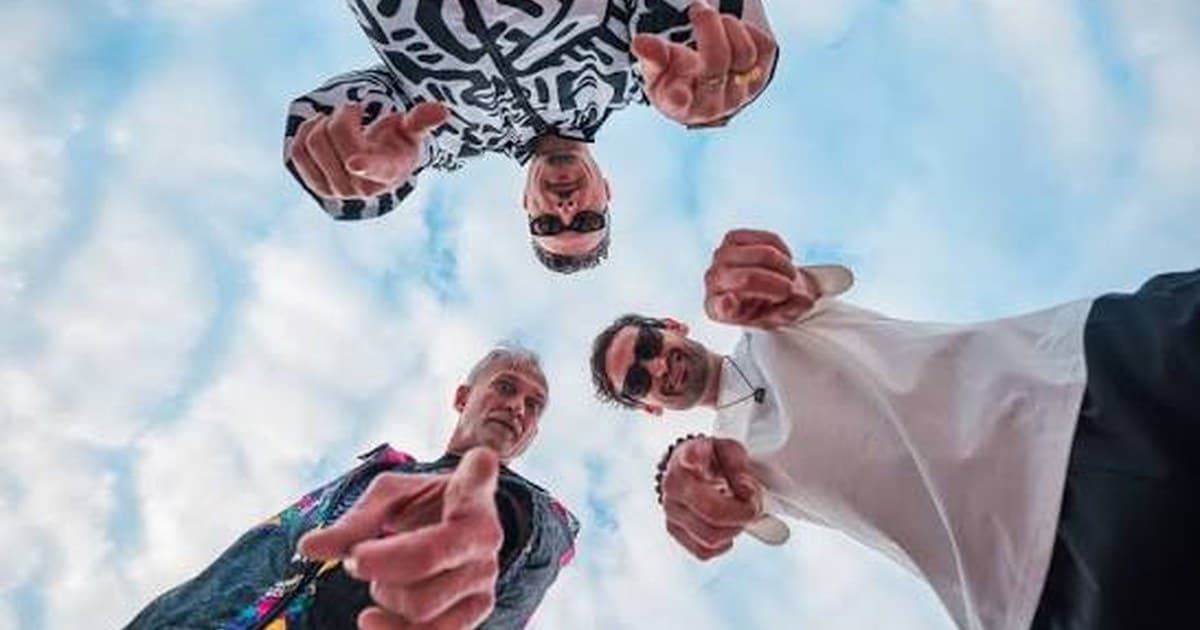 The Desert Hearts crew photographed from below against a bright blue sky, hands reaching toward the camera.