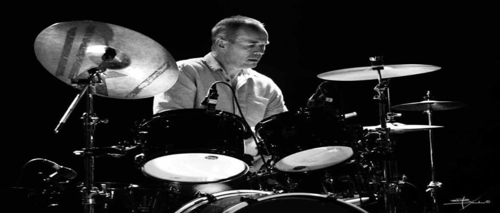 Egil Vollan at the drum kit in a black-and-white performance photograph, looking down at the toms.