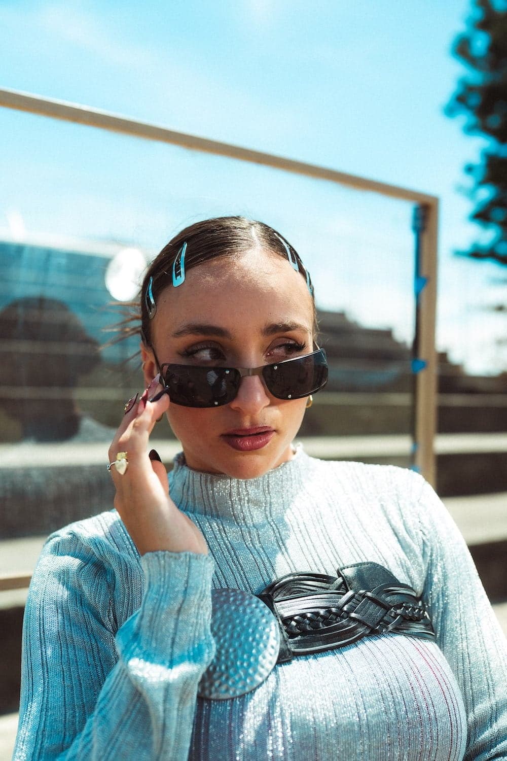 GAZAL in dark sunglasses and a pale blue knit, with blue clips in her hair.