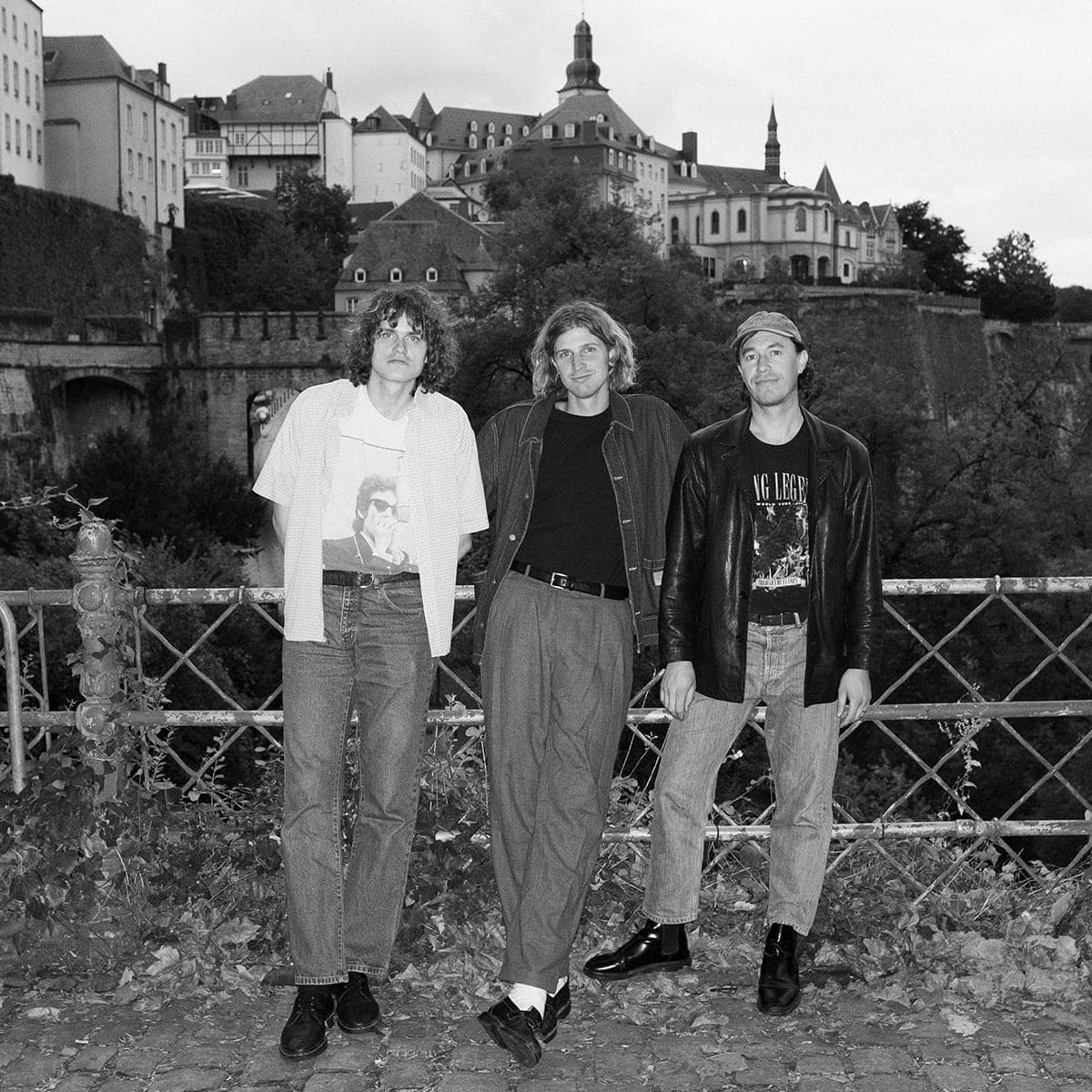 The three members of GOBLYNS in black and white, standing at a railing above an old town.