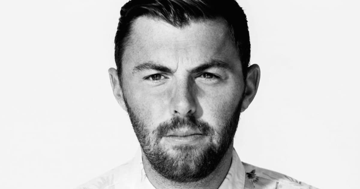 Black-and-white portrait of Goldroom looking directly at the camera in a light patterned shirt against a plain background.