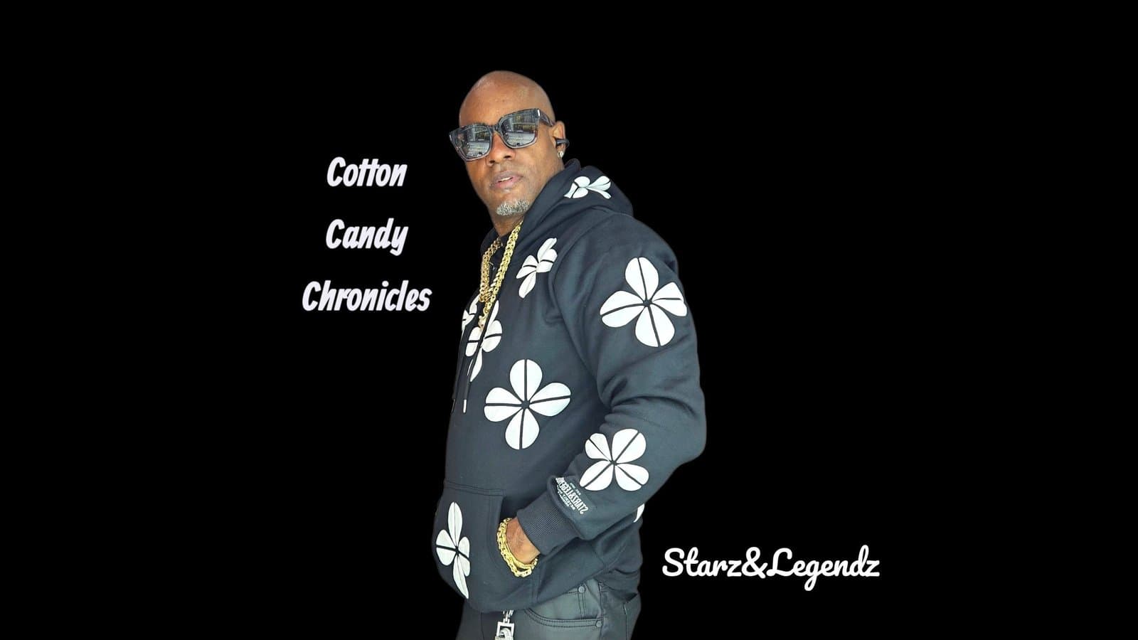 Starz&Legendz in sunglasses, a gold chain, and a black hoodie covered in white four-petal flowers, with the words Cotton Candy Chronicles beside him.