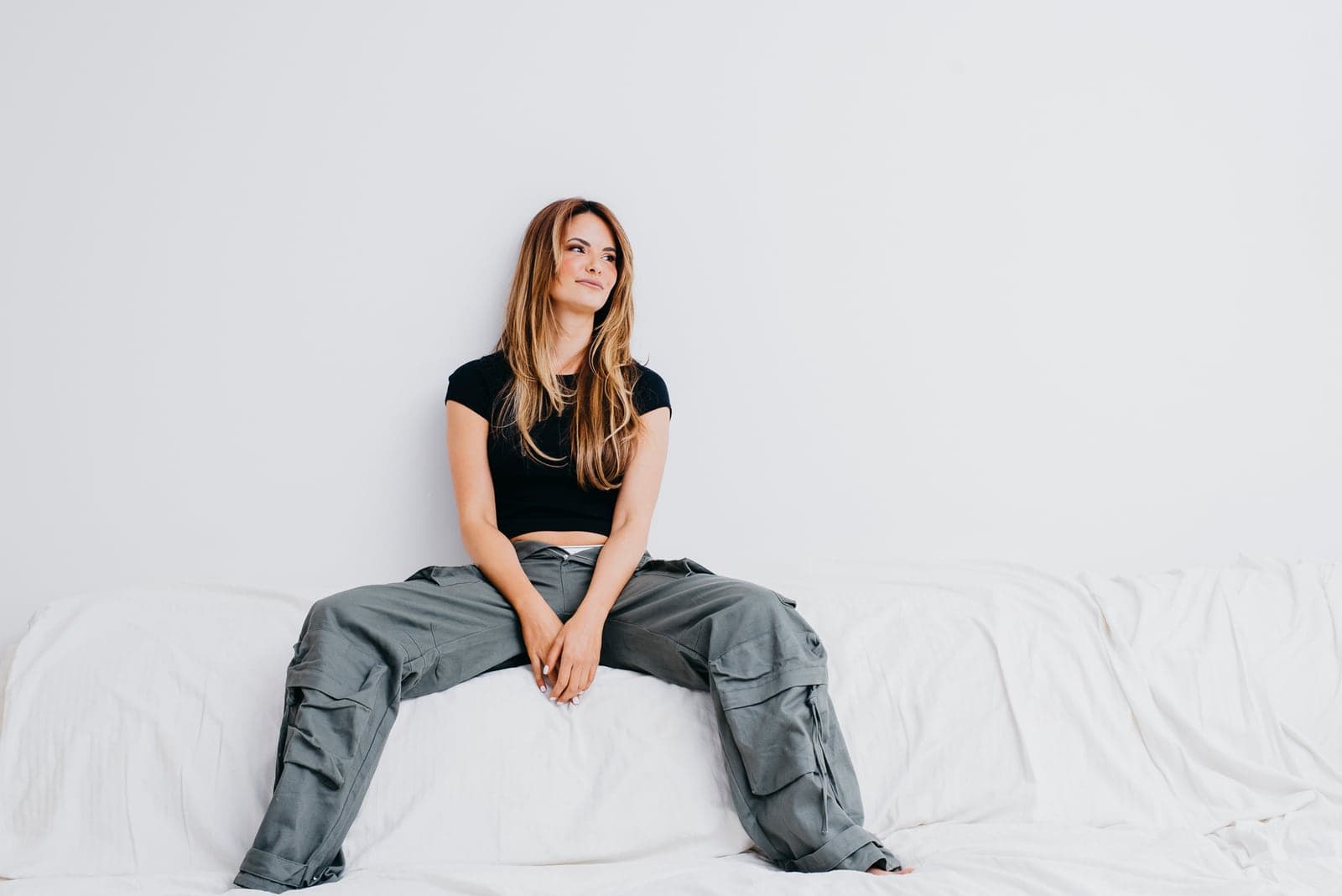 Terra Renae sitting on a white sofa in a black tee and grey cargo pants.