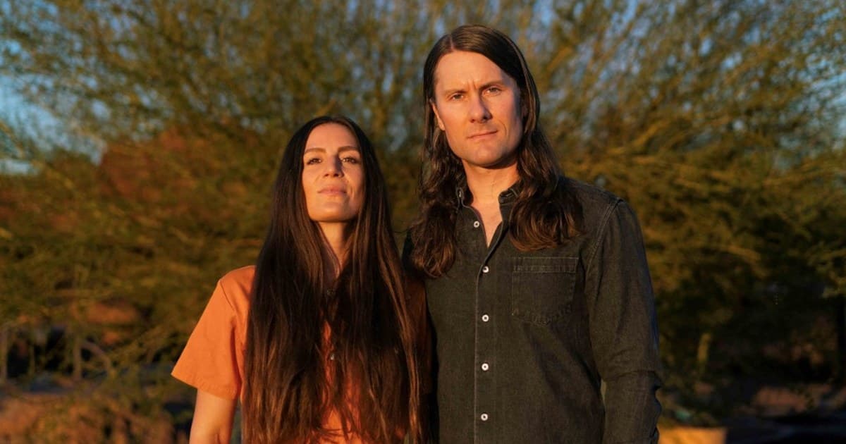The Bergamot, a husband-and-wife duo, standing together outdoors in warm golden evening light among desert trees.