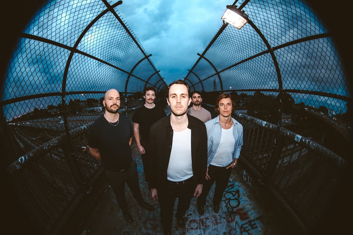 The five members of The Upsides standing on a caged pedestrian footbridge at dusk.