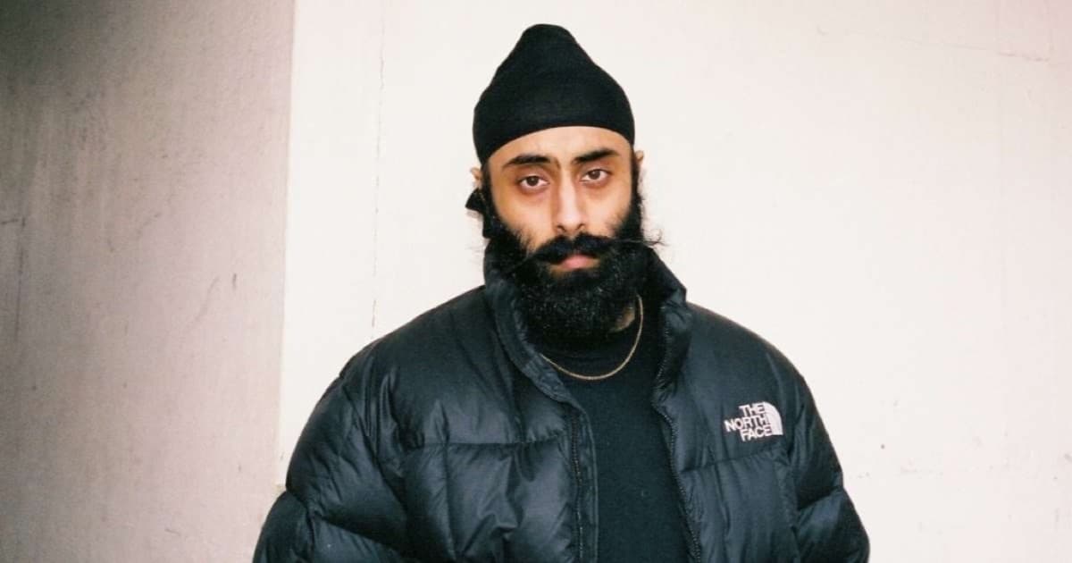 Yung Singh photographed against a pale concrete wall, wearing a black beanie and a black puffer jacket.