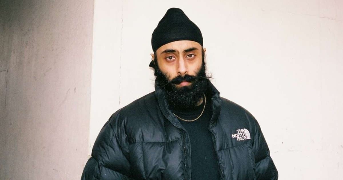 Yung Singh photographed against a pale concrete wall, wearing a black beanie and a black puffer jacket.
